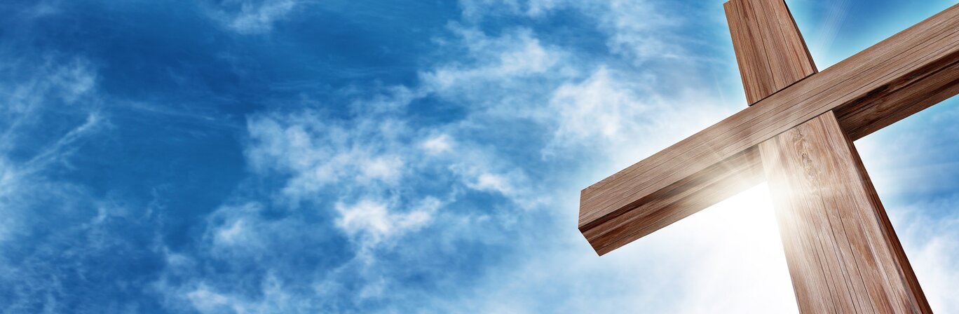 Auf dem Bild ist blauer Himmel zu sehen mit einem großen Holzkreuz im Vordergrund | © Adobe Stock - Balazs