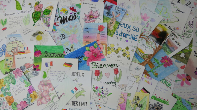 Viele gemalte Karten und Bilder mit der Aufschrift "Bienvenue a Mering", was französisch ist und heißt: Willkommen in Mering